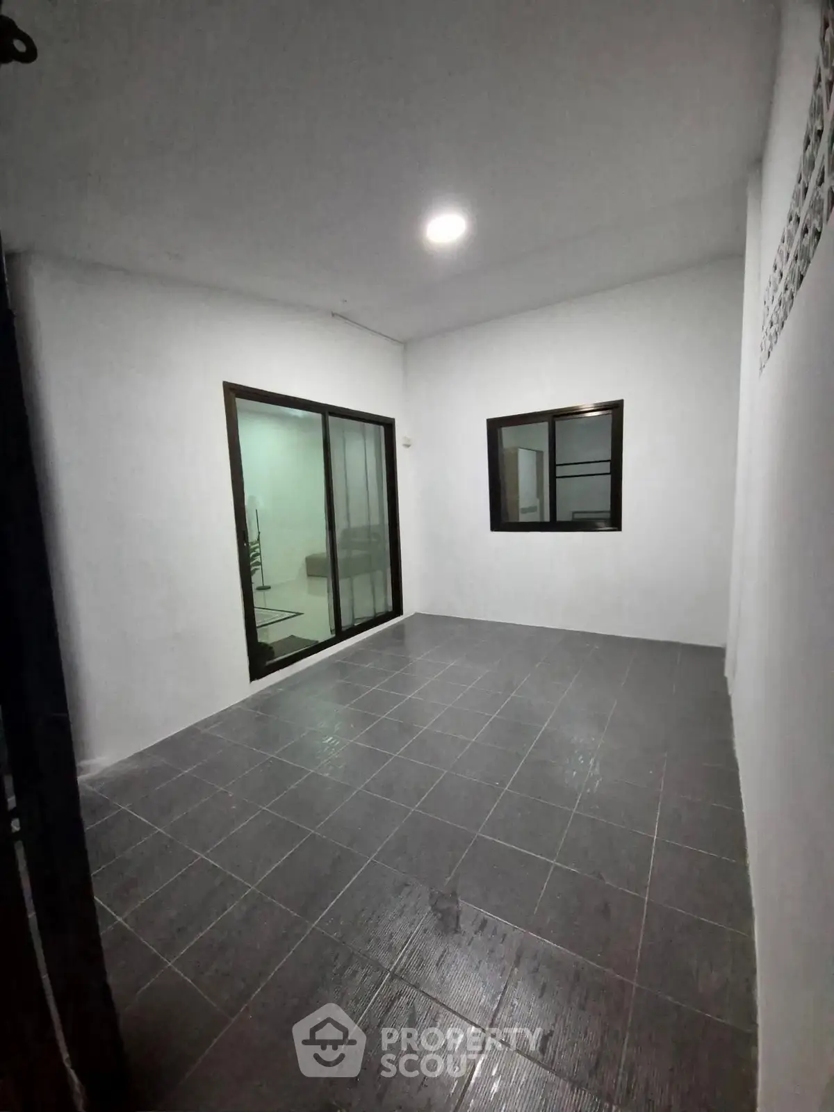 Spacious tiled room with sliding glass door and window, ideal for versatile use.