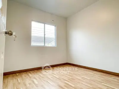Spacious empty room with wooden flooring and natural light from window.