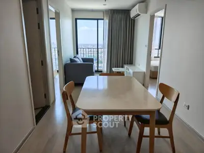 Modern apartment interior with dining area and living room featuring a large window with city view.