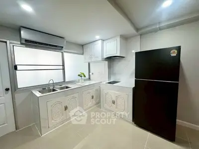 Modern kitchen with sleek white cabinetry and black refrigerator, featuring a minimalist design and ample natural light.