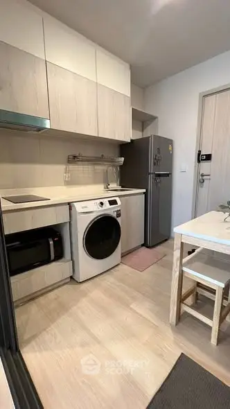Modern kitchen with sleek appliances and wooden cabinetry, featuring a washing machine and fridge.