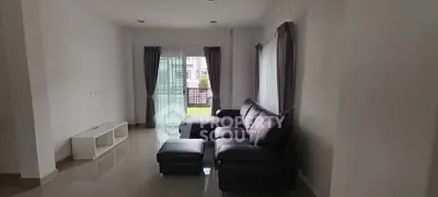 Spacious living room with modern black leather sofa and large windows for natural light.