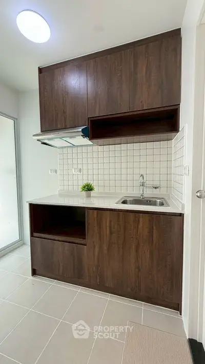 Modern kitchen with dark wood cabinets and sleek white countertops in a stylish apartment.