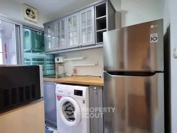 Compact kitchen with modern appliances including fridge, washing machine, and microwave, featuring sleek cabinetry.