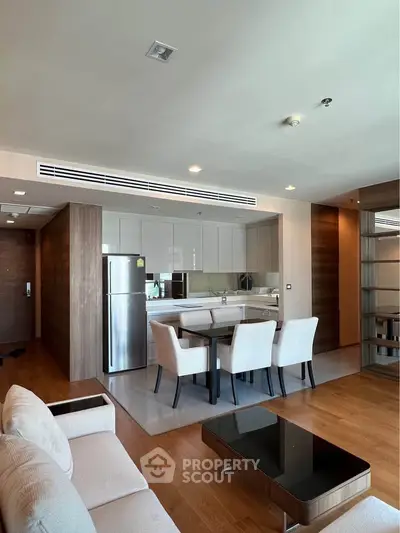 Modern open-plan living room with sleek kitchen and dining area, featuring contemporary furniture and wooden flooring.