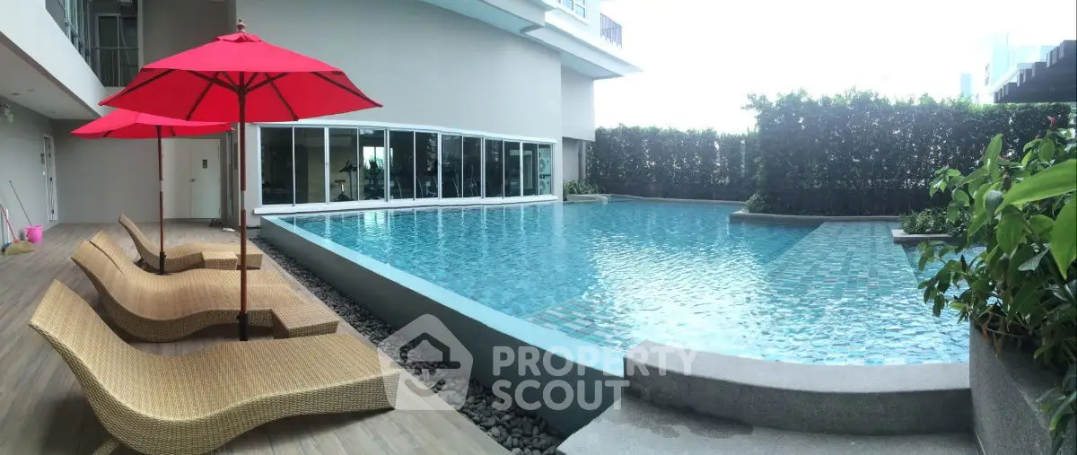 Luxurious modern pool area with stylish loungers and vibrant red umbrellas, perfect for relaxation.