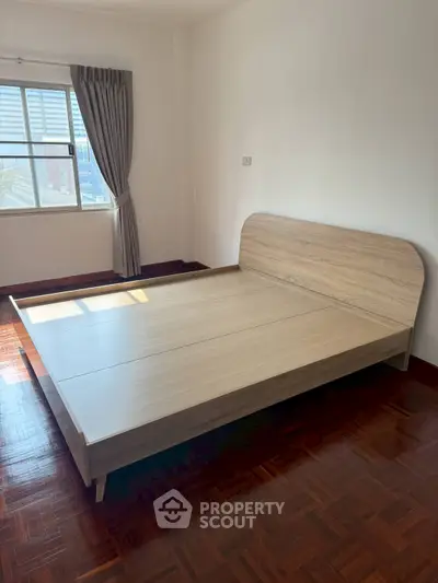 Spacious bedroom with wooden bed frame and large window offering city views.