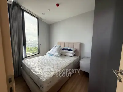 Modern bedroom with large window and city view, featuring a comfortable bed and sleek design.
