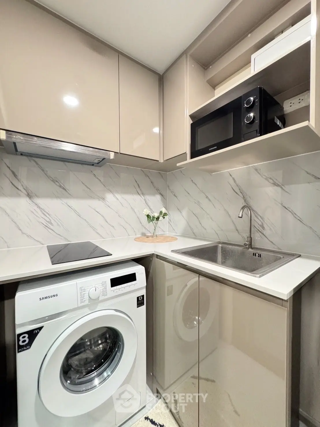Modern compact kitchen with washing machine and microwave, sleek cabinetry, and marble backsplash.
