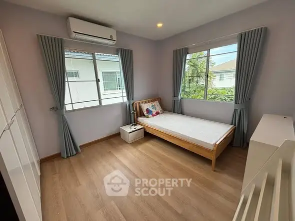 Cozy bedroom with wooden flooring, single bed, and large windows for natural light.