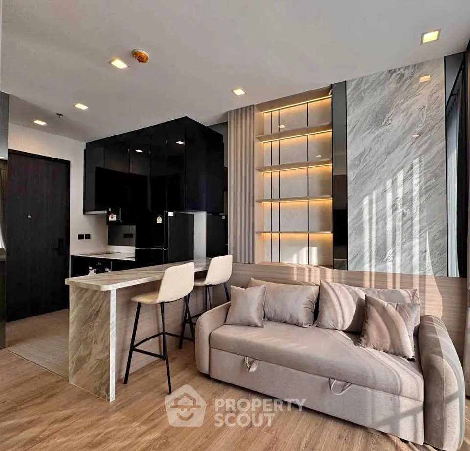 Modern living room with stylish sofa and open kitchen layout, featuring sleek black cabinets and elegant lighting.