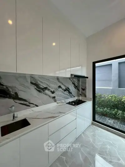 Sleek modern kitchen with marble backsplash and large window view