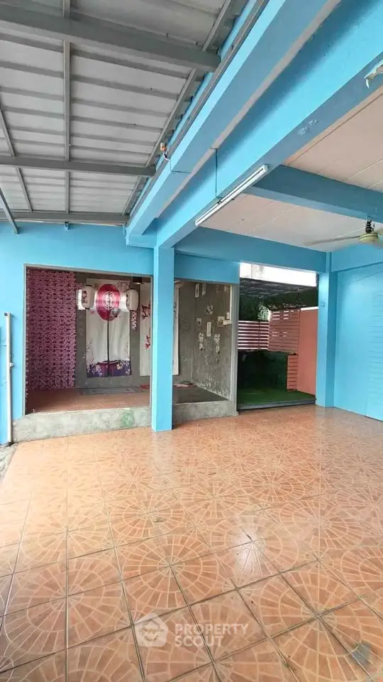 Spacious covered outdoor area with tiled flooring and vibrant blue walls, perfect for versatile use.