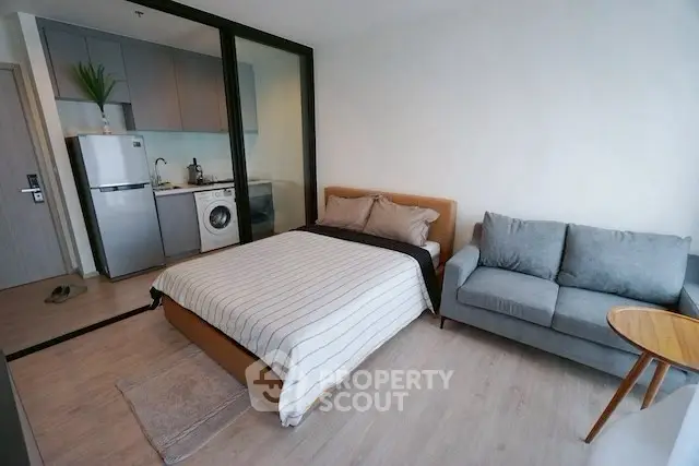 Modern studio apartment with cozy bed, compact kitchen, and stylish sofa.