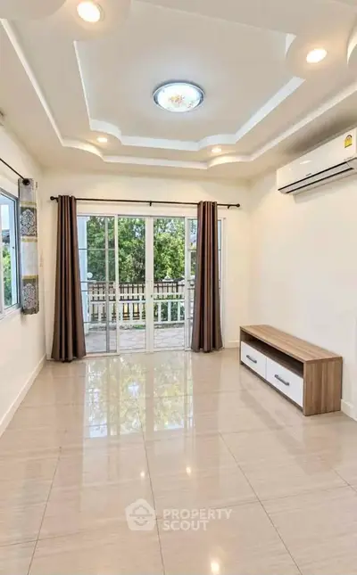 Spacious living room with modern ceiling design and large windows opening to a balcony.