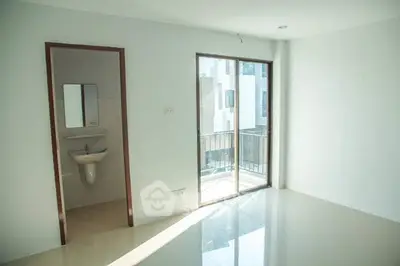 Bright empty room with balcony access and adjacent bathroom in modern apartment.