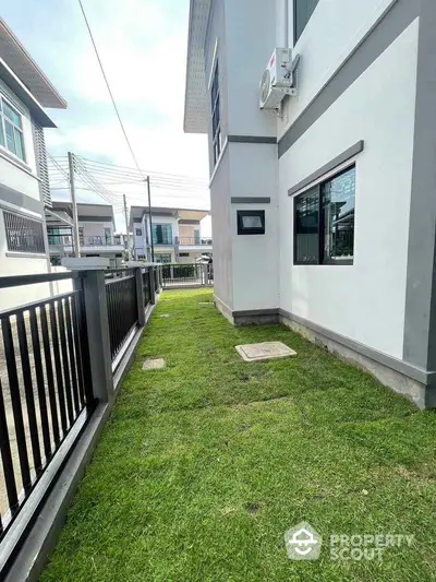 Modern residential building exterior with green lawn and sleek fence design