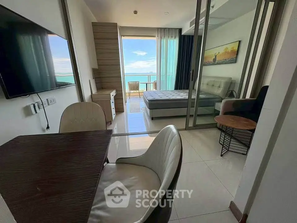 Modern apartment with ocean view, featuring a cozy living area and stylish bedroom separated by glass doors.