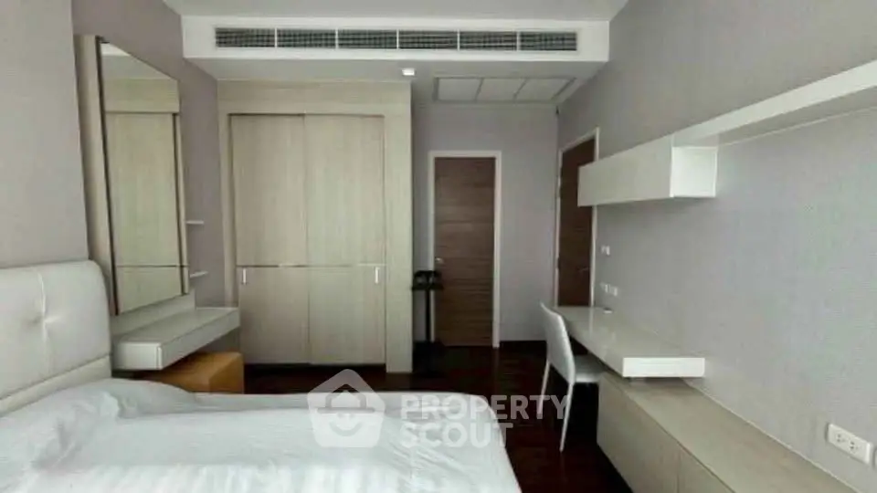 Modern bedroom with sleek furniture and neutral tones, featuring a built-in wardrobe and study desk.