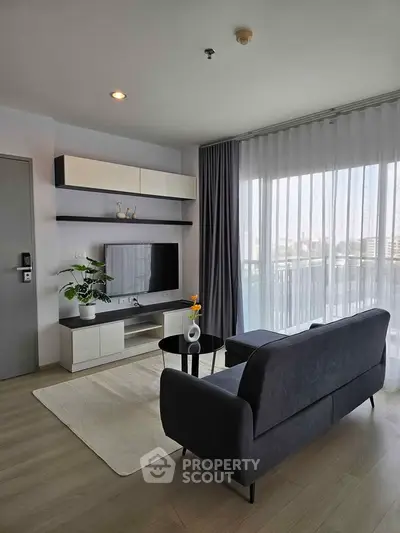 Modern living room with sleek furniture and large window offering natural light and city view.