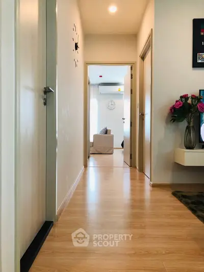 Modern hallway with wooden flooring leading to a bright living area, featuring stylish decor and wall clock.