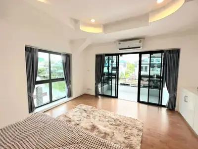 Spacious bedroom with large windows and balcony overlooking serene neighborhood.