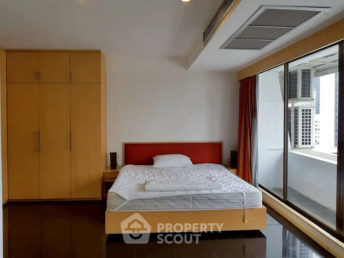 Spacious bedroom with large window and modern furnishings in urban apartment