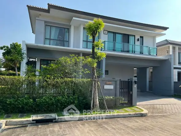 Modern two-story house with balcony and lush greenery in a serene neighborhood.
