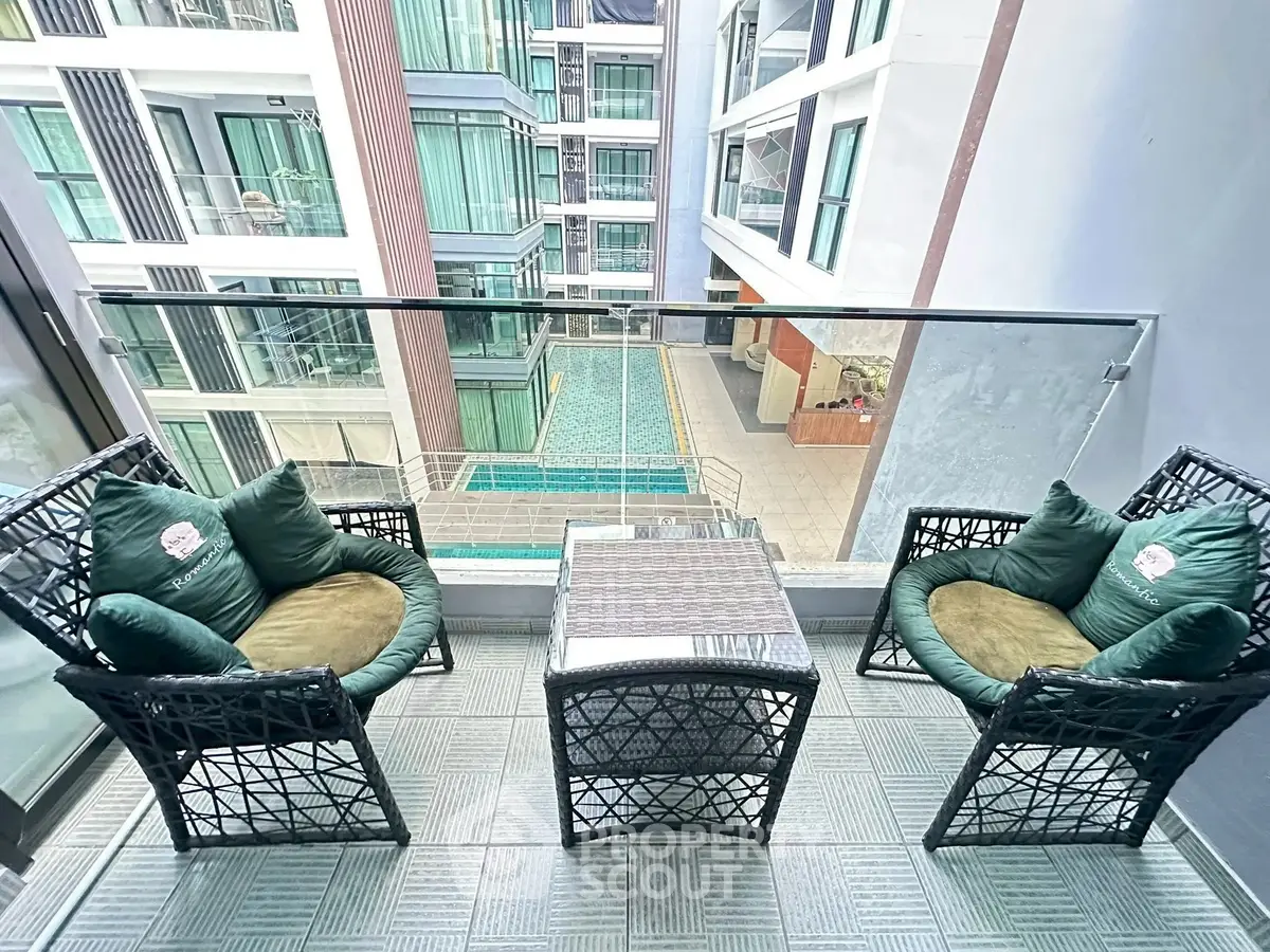 Modern balcony with stylish seating overlooking a pool in a contemporary apartment complex.