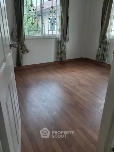 Spacious empty room with wooden flooring and elegant curtains, perfect for customization.