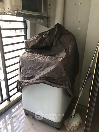 Compact washing machine on balcony with mop and cover, ideal for urban apartments.