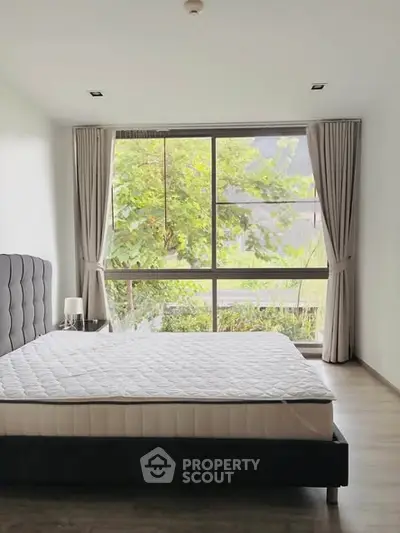 Spacious bedroom with large window offering lush green views, perfect for relaxation and comfort.