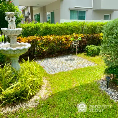 Charming garden with lush greenery and elegant stone fountain in modern residential area.