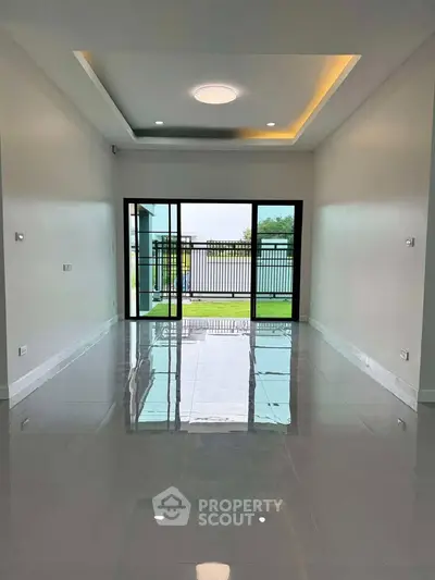 Spacious modern living room with large glass doors opening to a garden view, featuring sleek tile flooring.