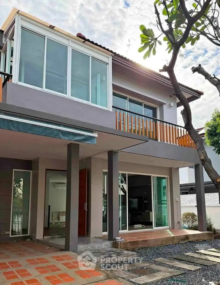 Modern two-story house with large windows and balcony, featuring sleek design and spacious outdoor area.