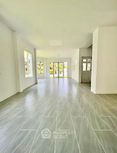 Spacious open-plan living room with large windows and tiled flooring, perfect for natural light and modern living.
