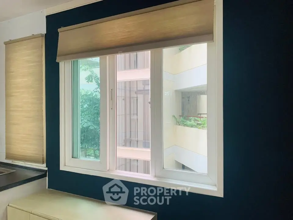 Modern window with beige blinds overlooking lush greenery and building exterior.