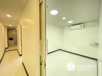 Bright and modern hallway in a residential building with clean white tiles and well-lit interior, featuring a secure entrance door and air conditioning unit.