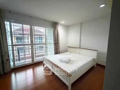 Spacious bedroom with large windows and wooden flooring in modern apartment.