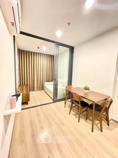 Modern dining area with wooden table and chairs, adjacent to cozy living room with glass partition.
