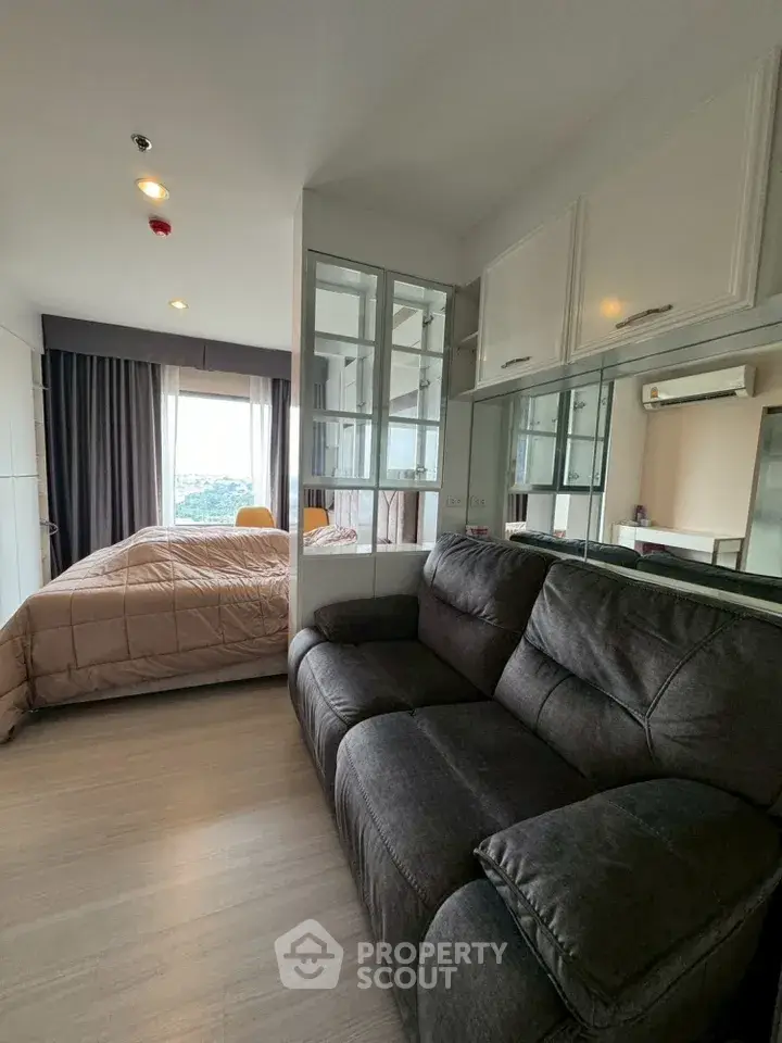 Modern studio apartment with cozy living area and large windows offering a stunning city view.
