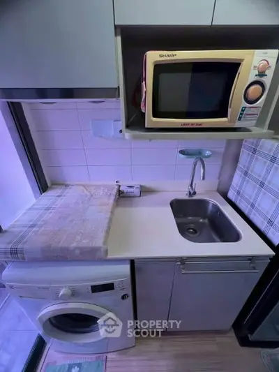 Compact kitchen with washing machine, microwave, and sink in modern apartment.