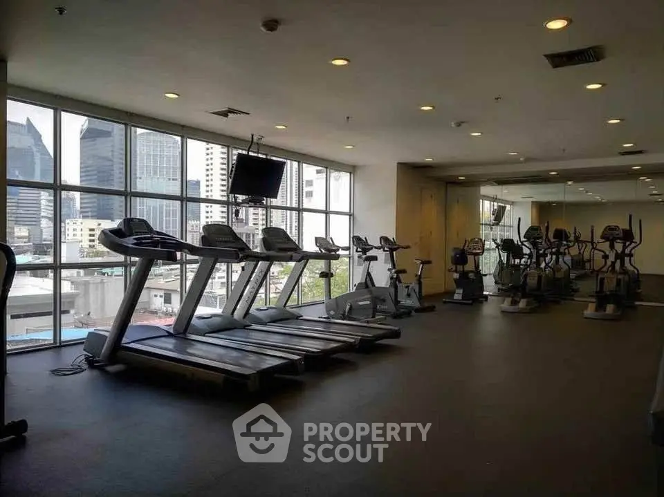 Spacious gym with modern equipment and city view in luxury building.