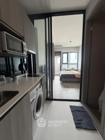 Modern apartment with sleek kitchen and cozy bedroom, featuring a washing machine and city view.