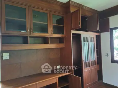 Spacious wooden storage unit with glass cabinets and built-in desk in a well-lit room.