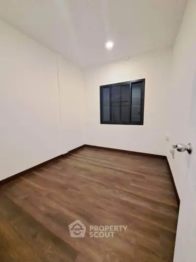 Spacious empty room with wooden flooring and large window, perfect for customization.