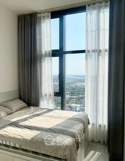 Bright bedroom with large window offering stunning city view, modern decor and cozy ambiance.
