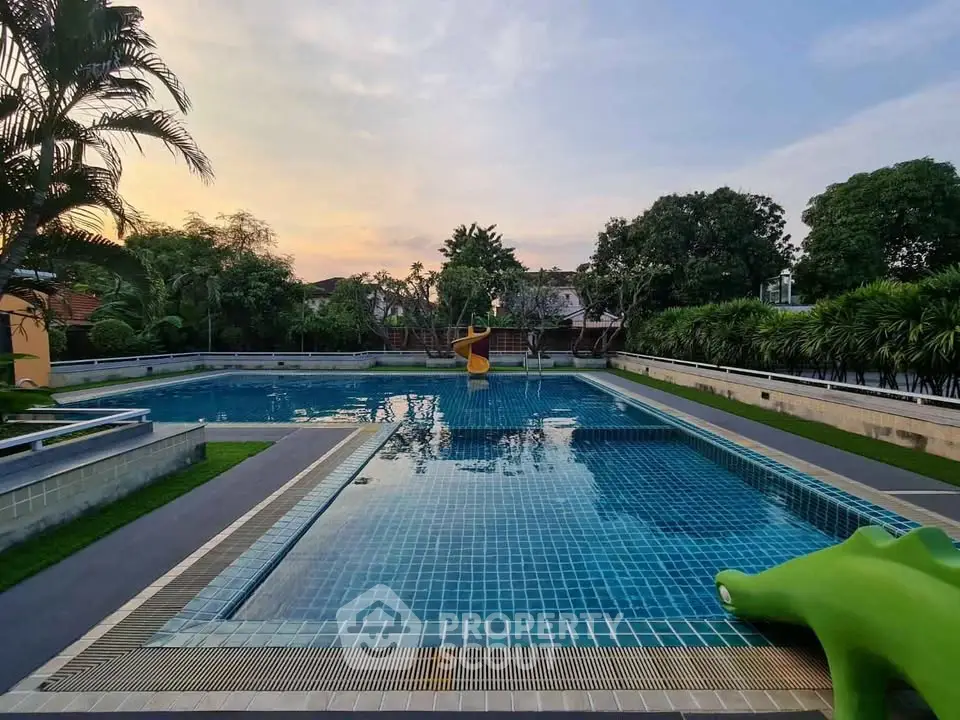 Luxurious outdoor swimming pool with slide and lush greenery, perfect for relaxation and leisure.