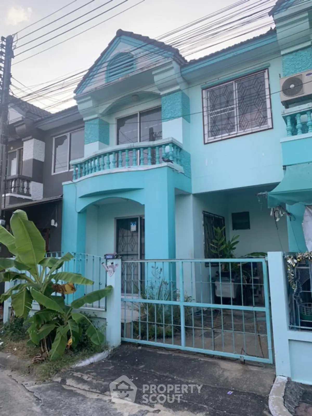 Charming turquoise townhouse with gated entrance and balcony in a serene neighborhood.