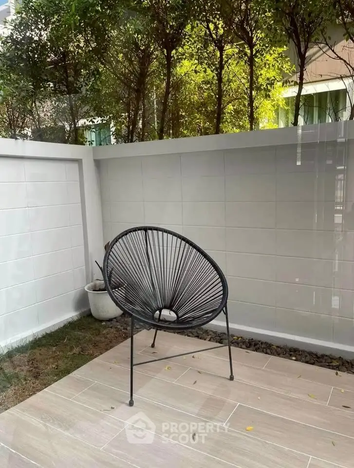 Charming outdoor patio with modern chair and lush greenery, perfect for relaxation and entertaining.